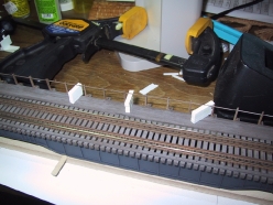 Plastic blocks were used to hold the piano wire railing at the proper height for gluing. Plastic blocks were used to hold the piano wire railing at the proper height for gluing.